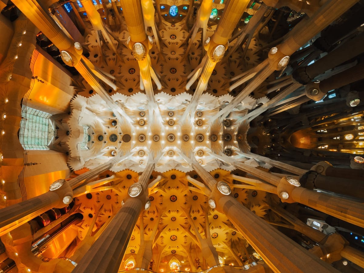 Blick nach oben in das Deckengewölbe der Sagrada Família mit buntem Fensterlicht