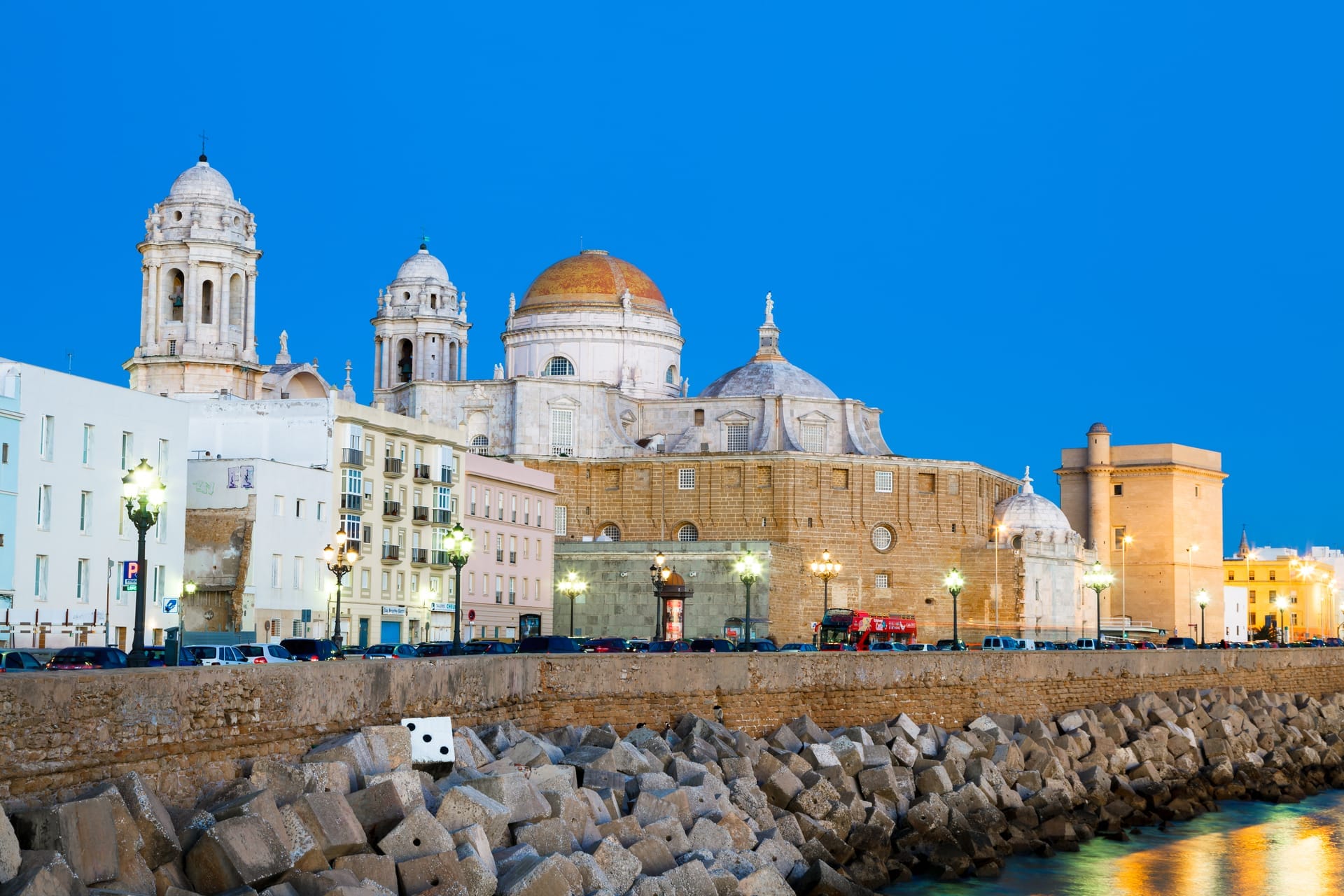Die Kathedrale von Cádiz mit ihrer goldgelben Kuppel in der blauen Stunde, davor die Uferbefestigung am Atlantik