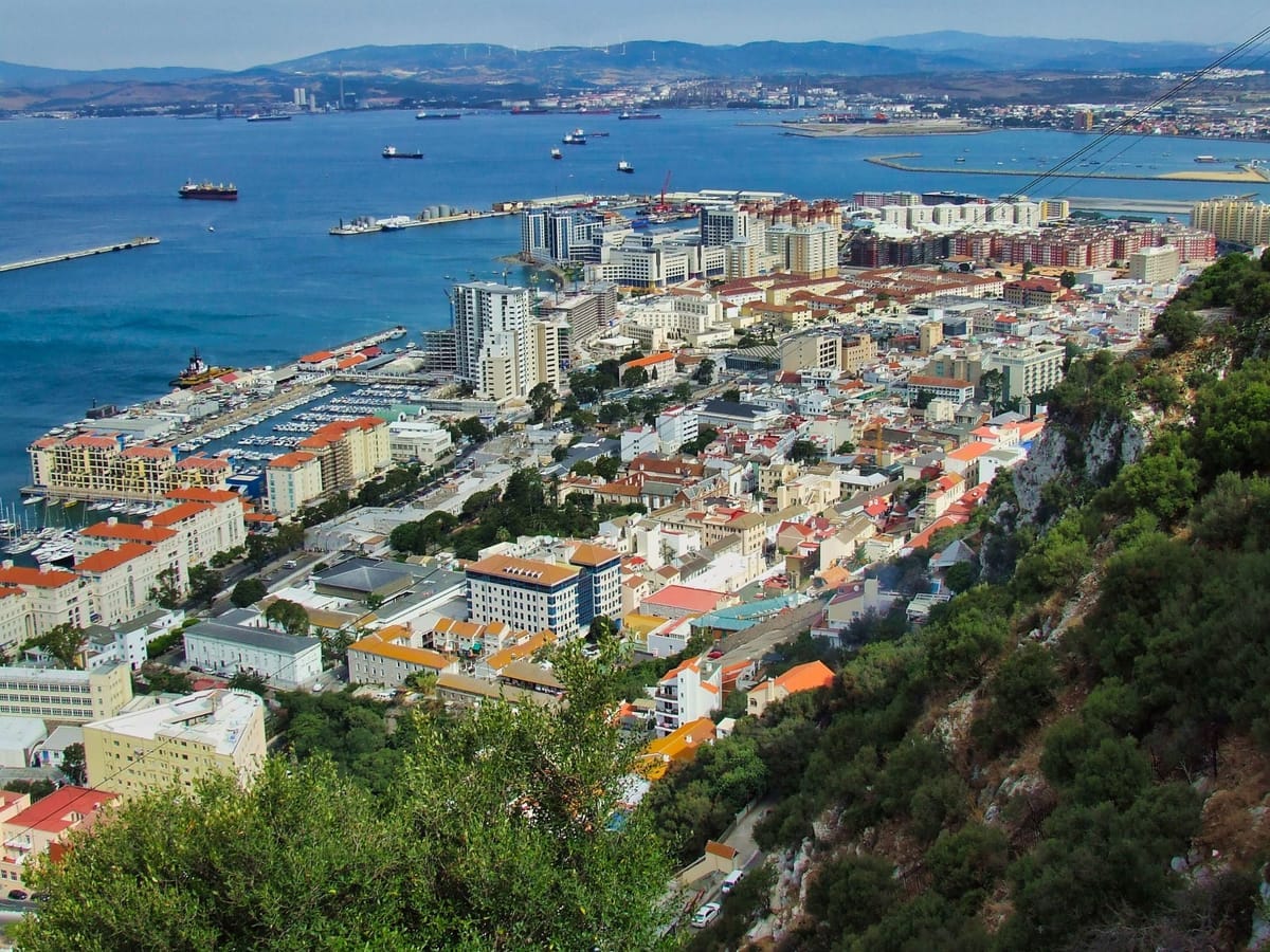 Blick von der Seilbahn über die dicht bebaute Stadt Gibraltar, die Marina und die Bucht von Algeciras mit ankernden Frachtschiffen