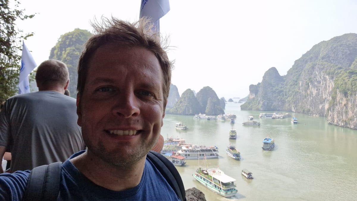 André vom Kreuzfahrt-Guide auf einem Aussichtspunkt über der Halong-Bucht, dahinter Dutzende weiße Ausflugsboote zwischen den Karstfelsen