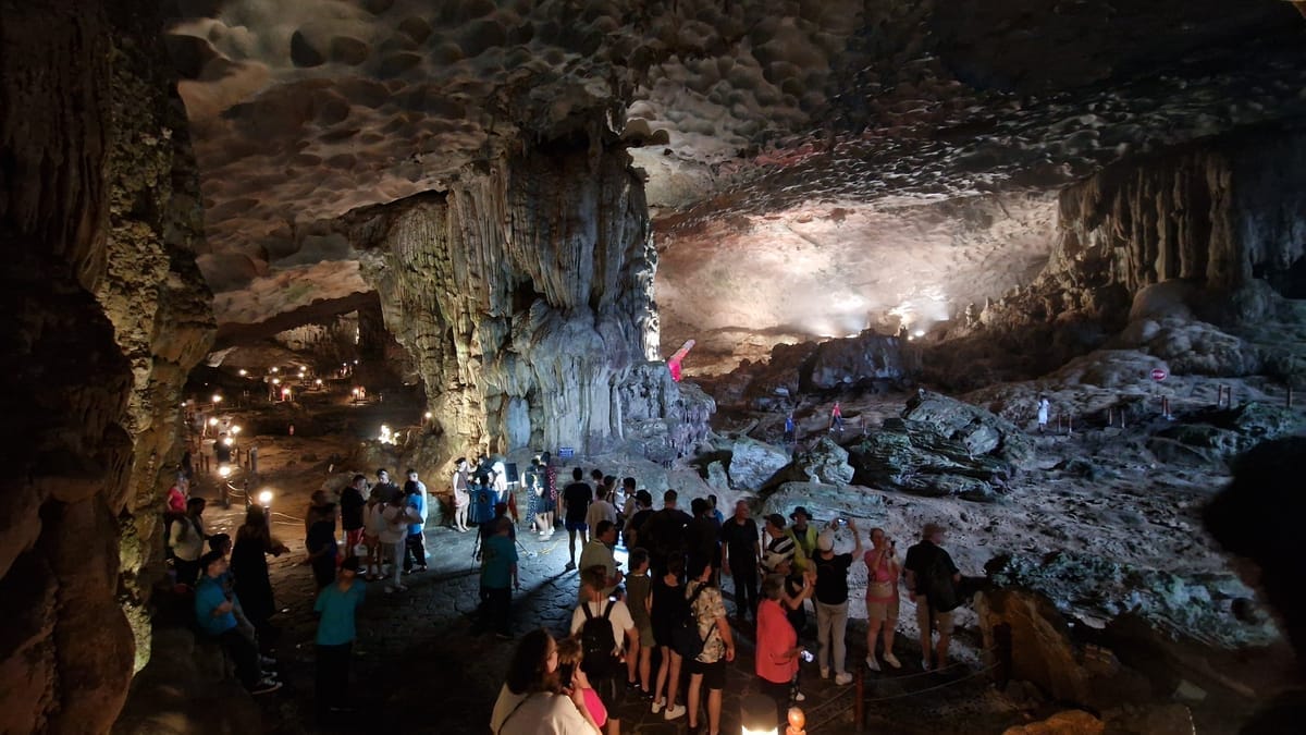 Weite, angestrahlte Tropfsteinhalle der Sung-Sot-Höhle mit mächtigen Kalksteinsäulen, im Vordergrund eine Besuchergruppe auf dem beleuchteten Rundweg