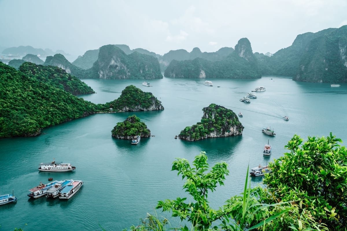 Blick von oben über die Karstinseln der Halong-Bucht mit mehreren Ausflugsbooten auf dem türkisfarbenen Wasser
