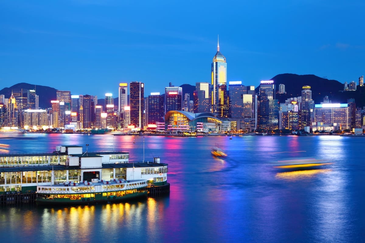 Eine grün-weiße Star Ferry liegt zur blauen Stunde am beleuchteten Fährpier, dahinter die Lichter der Skyline von Hongkong Island
