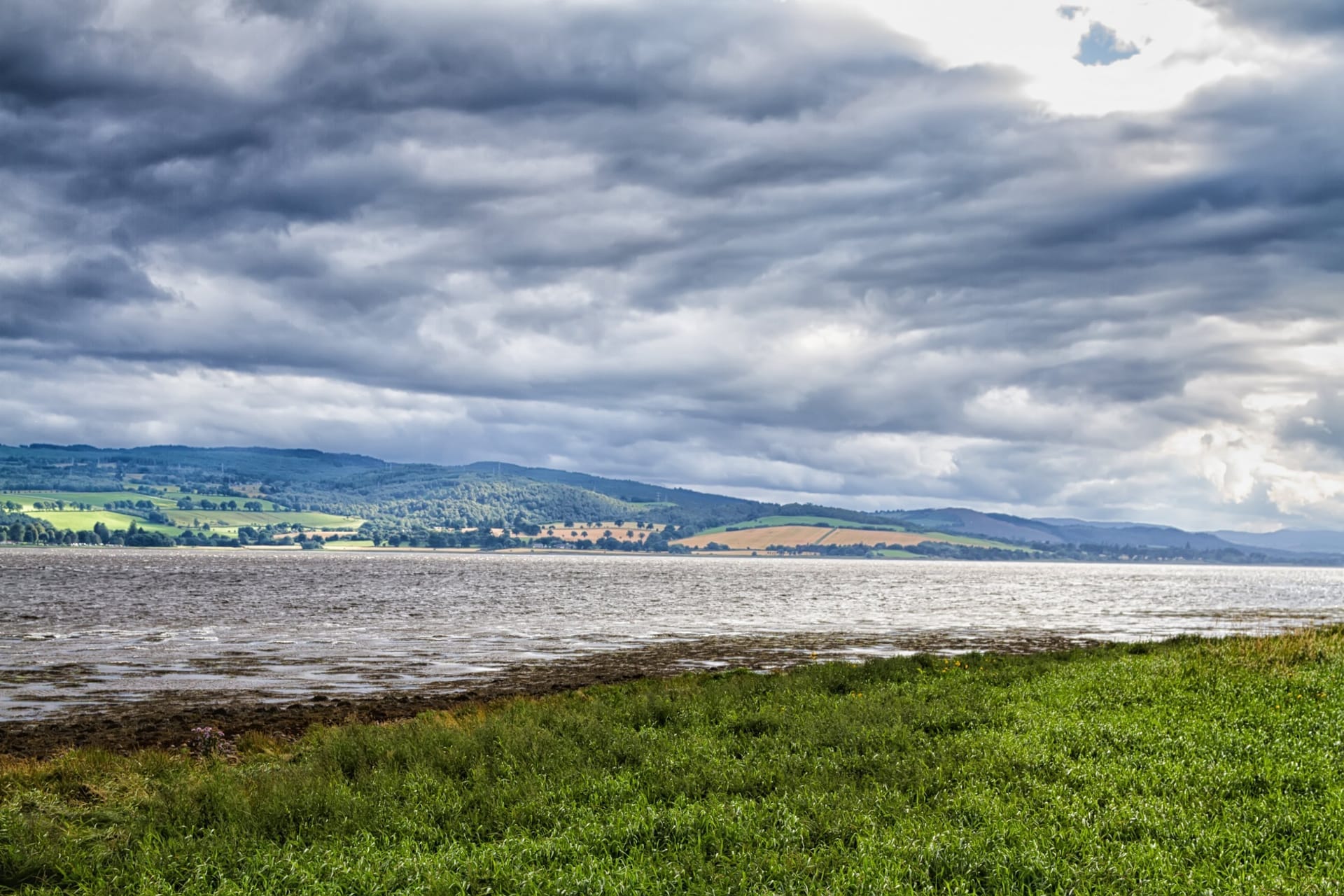 Der Cromarty Firth bei Invergordon mit grünen Hügeln der schottischen Highlands unter dramatischem Wolkenhimmel
