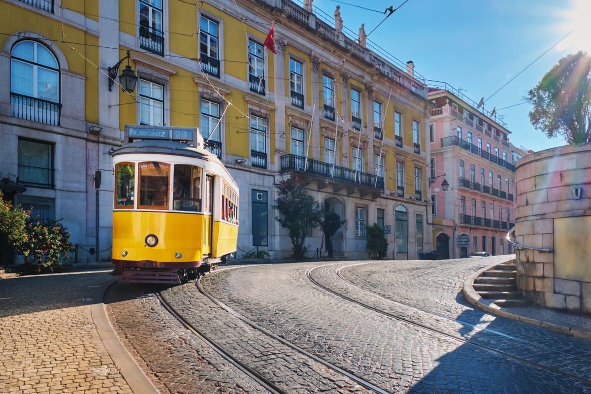 Die gelbe historische Straßenbahn der Linie 28 fährt durch eine enge Kopfsteinpflastergasse zwischen Häusern mit gelber und rosa Fassade