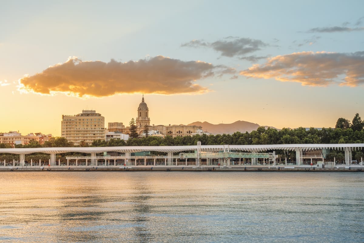 Uferpromenade Muelle Uno in Málaga im Abendlicht, das ruhige Hafenwasser spiegelt die Bebauung
