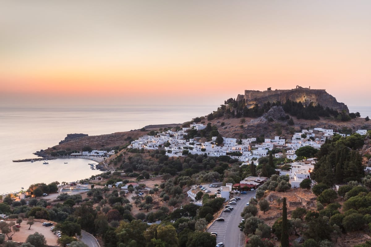 Weißes Dorf Lindos mit der Akropolis auf dem Felsen darüber und blauer Bucht