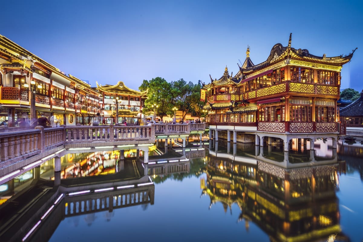 Beleuchtete traditionelle Gebäude am Yu-Garten in Shanghai spiegeln sich in der Dämmerung im Wasser