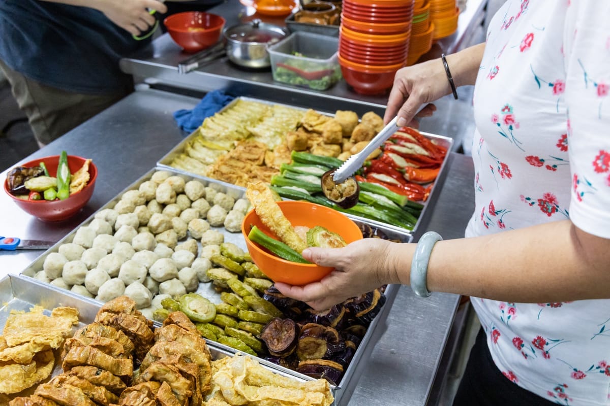 Verkäuferin an einem Hawker-Stand füllt frittierte Gemüse- und Tofustücke mit der Zange in eine Schale