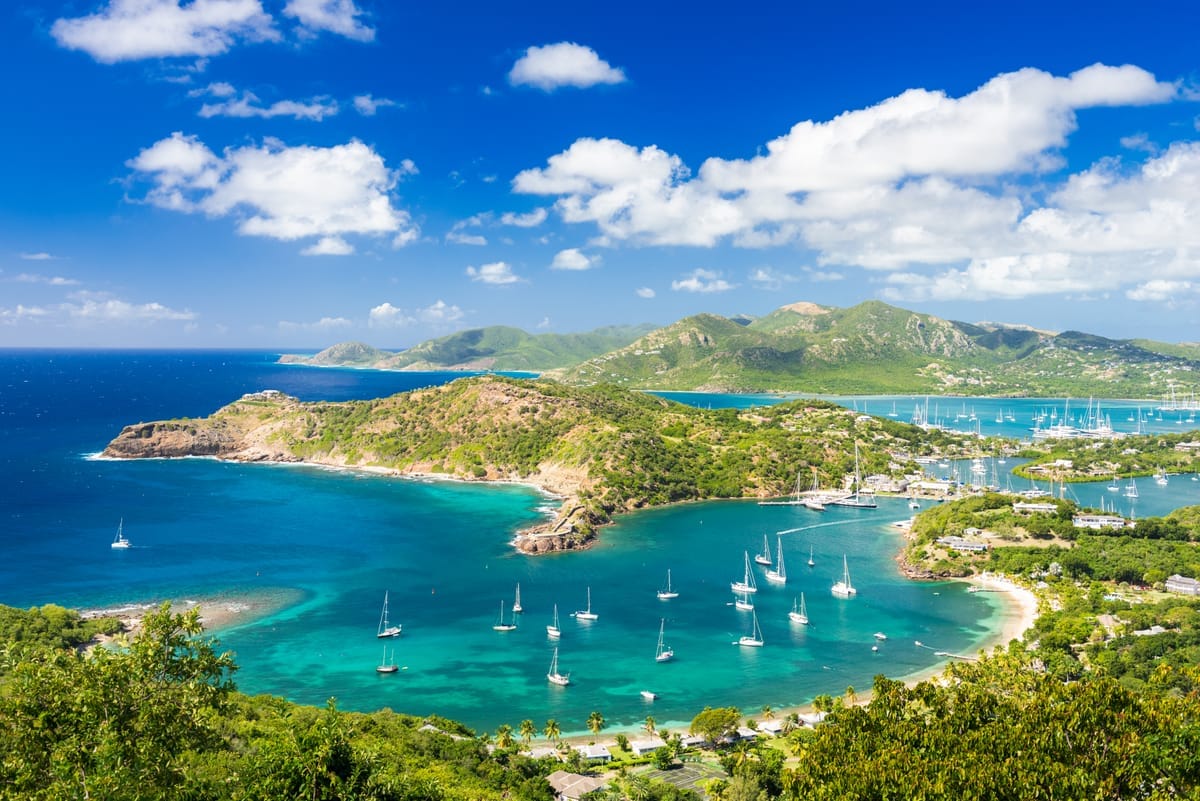Blick von oben über den English Harbour auf Antigua: türkisblaue, ineinander verschachtelte Buchten mit ankernden Segelyachten, umgeben von grünen Hügeln