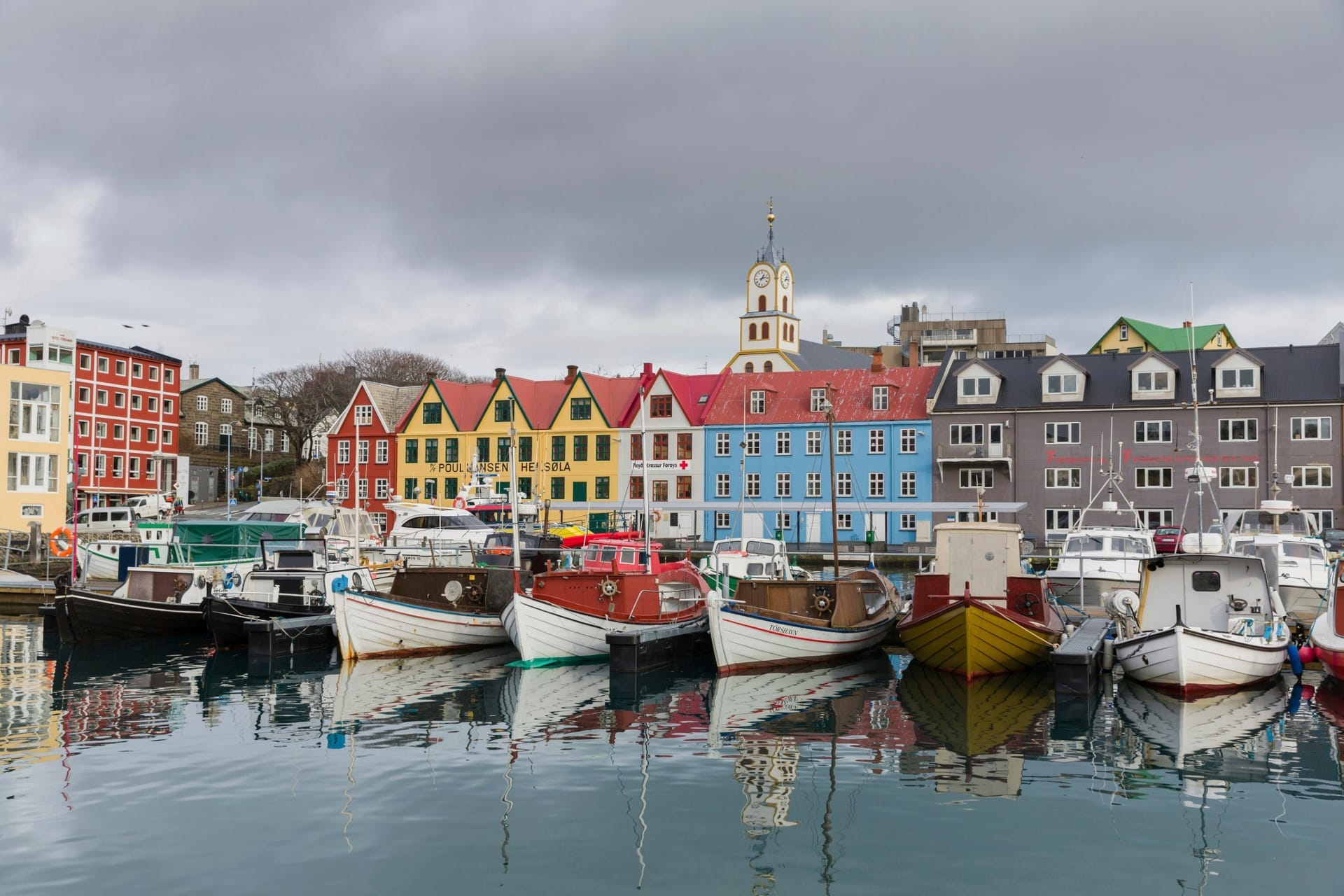 Bunte Häuser und Fischerboote im Hafenbecken Vágsbotnur von Tórshavn, im Hintergrund die Kirche mit Turmuhr