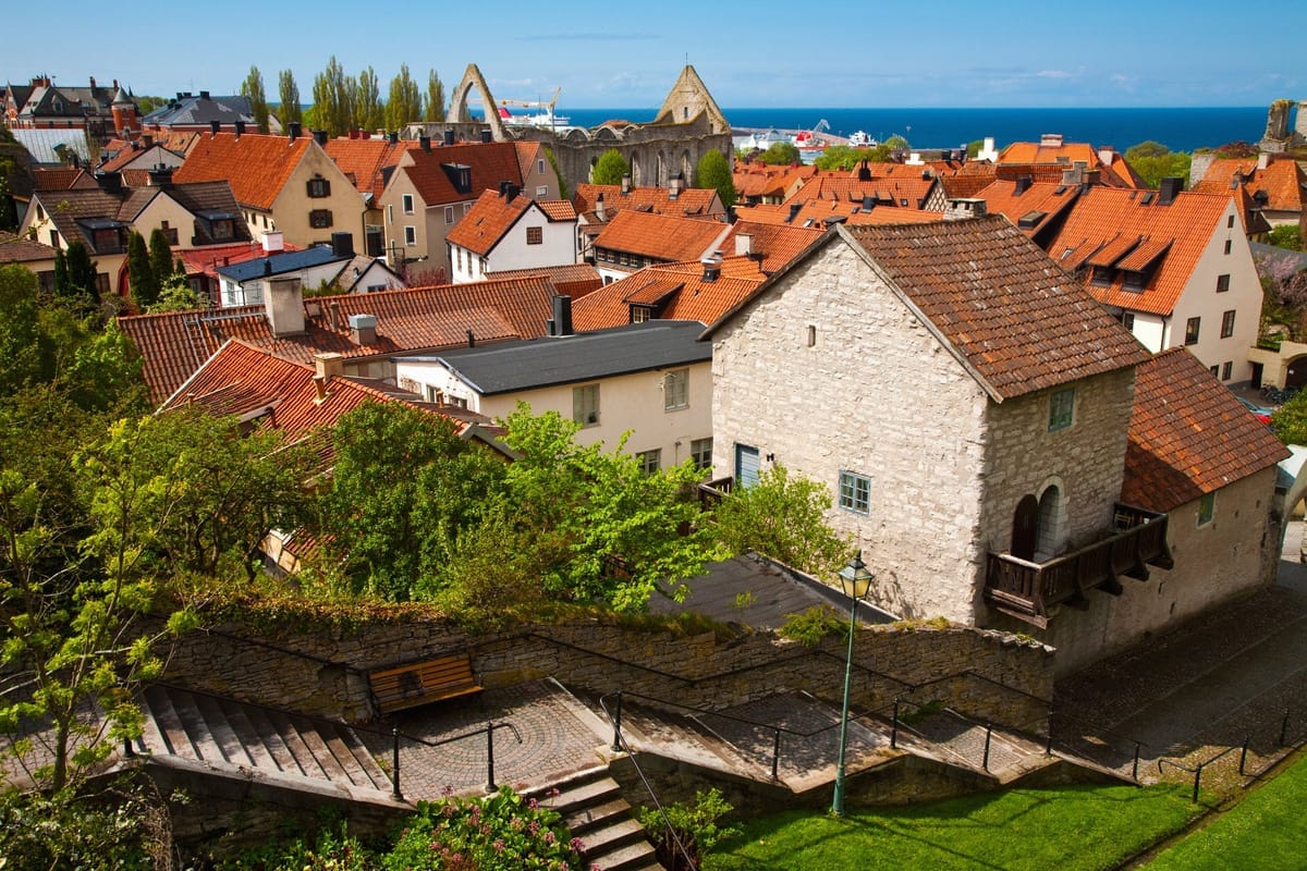 Blick über die Ziegeldächer der Visbyer Altstadt auf die Ruinen mittelalterlicher Kirchen und die Ostsee