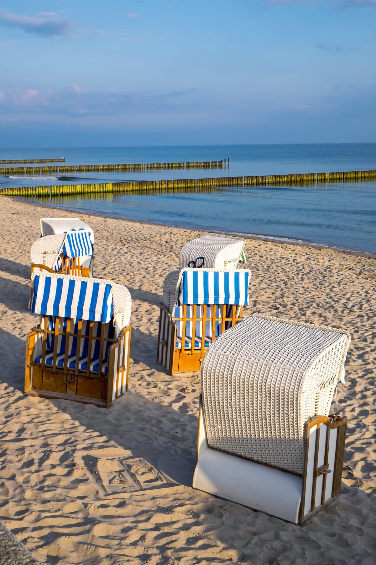 Weiße Strandkörbe am breiten Sandstrand von Warnemünde mit Ostsee im Hintergrund