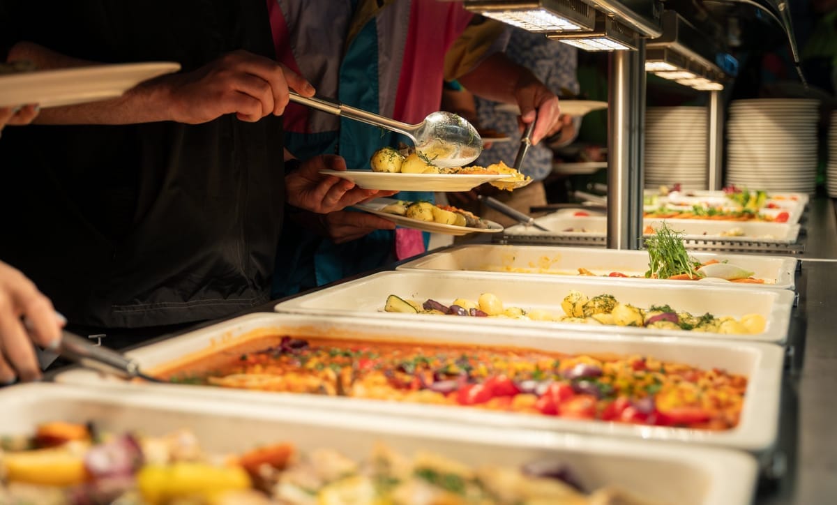 Gäste bedienen sich an einem Buffet mit mehreren gefüllten Warmhalteschalen