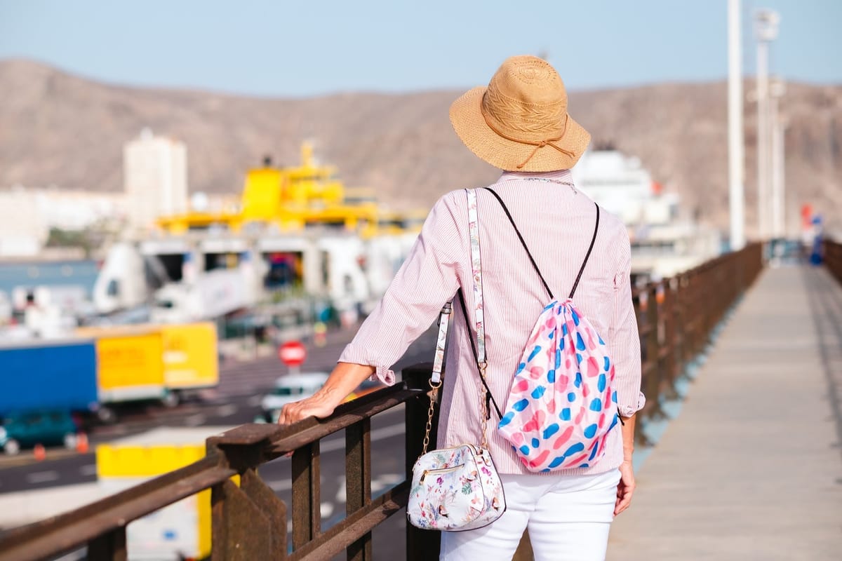 Reisende mit Sonnenhut und Rucksack blickt vom Pier auf ein Fährterminal im Hafen