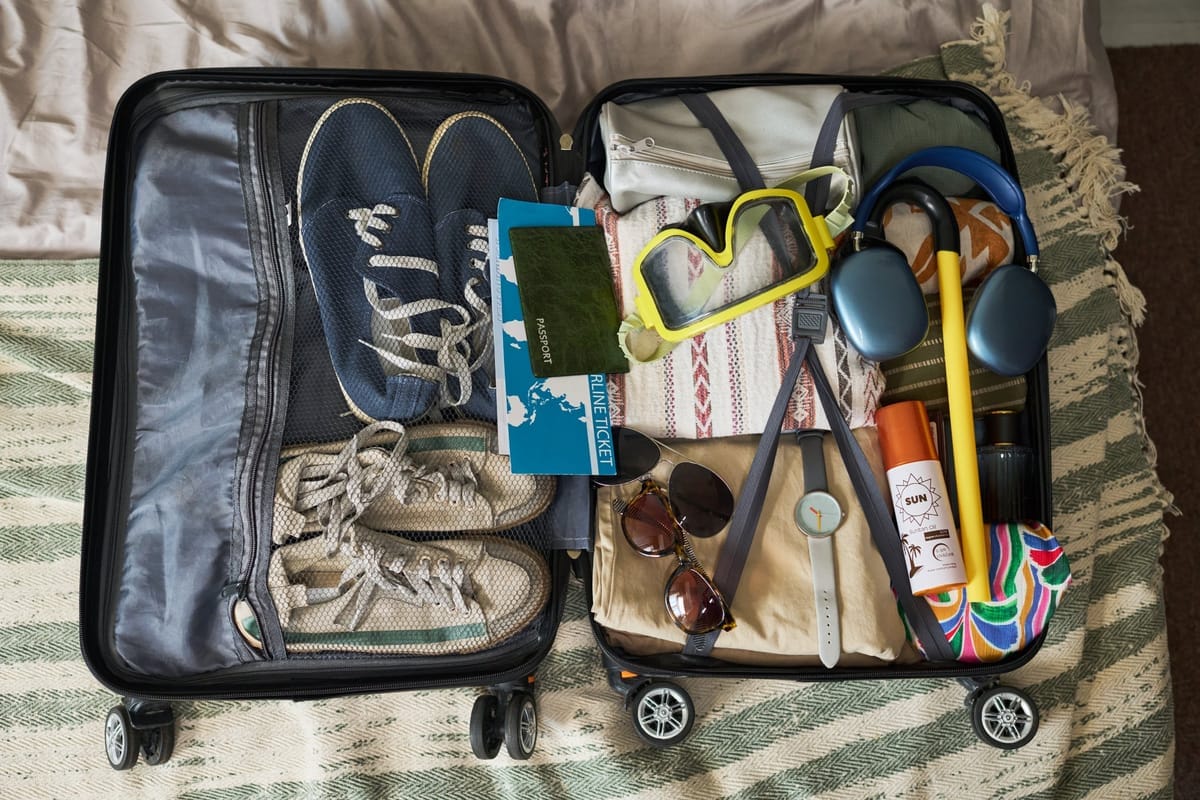 Geöffneter Koffer mit Schuhen, Reisepass, Sonnenbrille und Reiseaccessoires ordentlich verstaut