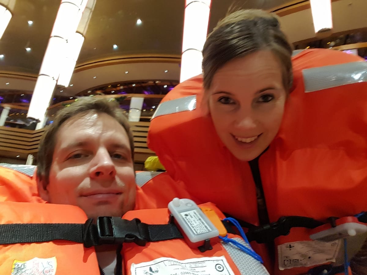 Zwei Passagiere mit angelegten orangefarbenen Rettungswesten an ihrer Sammelstation im Theater eines Kreuzfahrtschiffs