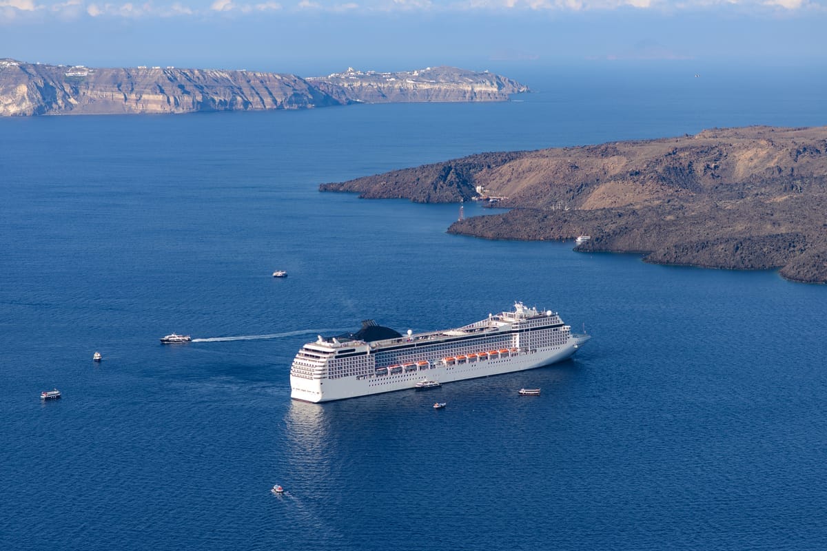 Ein Kreuzfahrtschiff liegt auf offenem Wasser vor der steil abfallenden Caldera-Küste von Santorini vor Anker