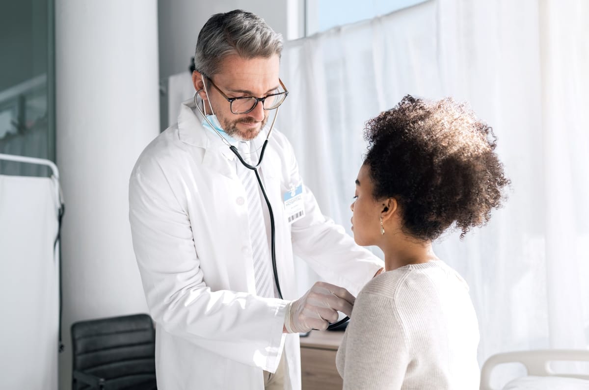 Arzt mit Stethoskop untersucht eine Patientin im Behandlungszimmer