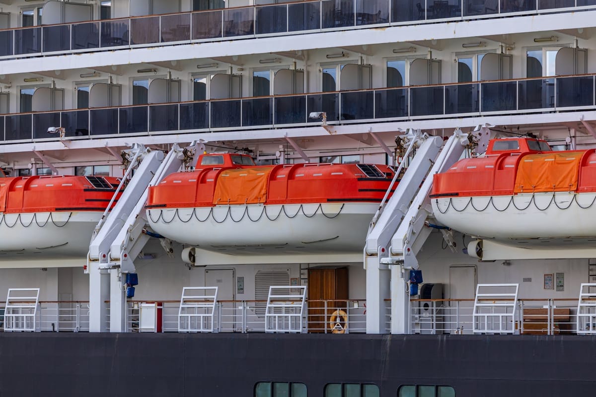 Reihe orangefarbener Rettungsboote hängt an Davits seitlich an einem Kreuzfahrtschiff