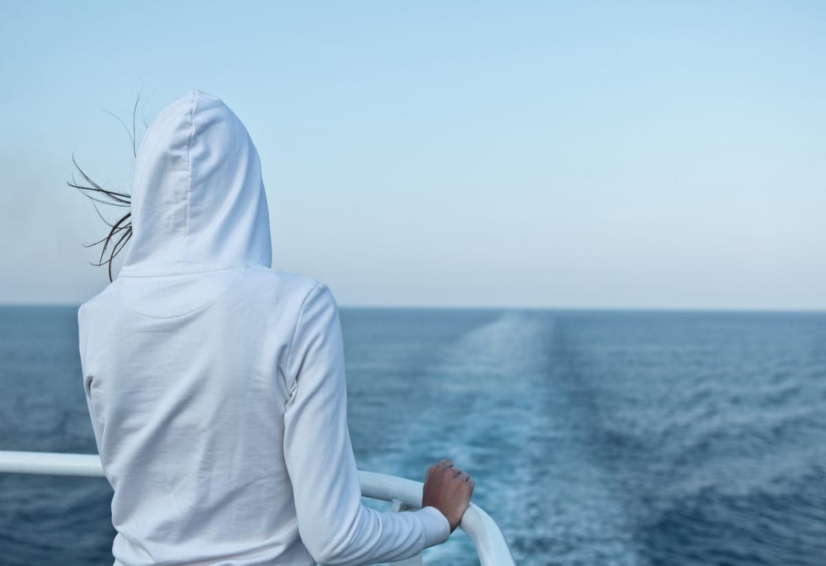 Person blickt vom Schiffsdeck über das Kielwasser zum Horizont