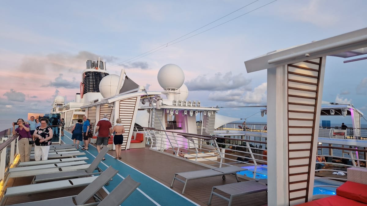 Sonnendeck eines Kreuzfahrtschiffs in der Abenddämmerung mit leeren Liegestühlen, Pool und rosa gefärbtem Himmel