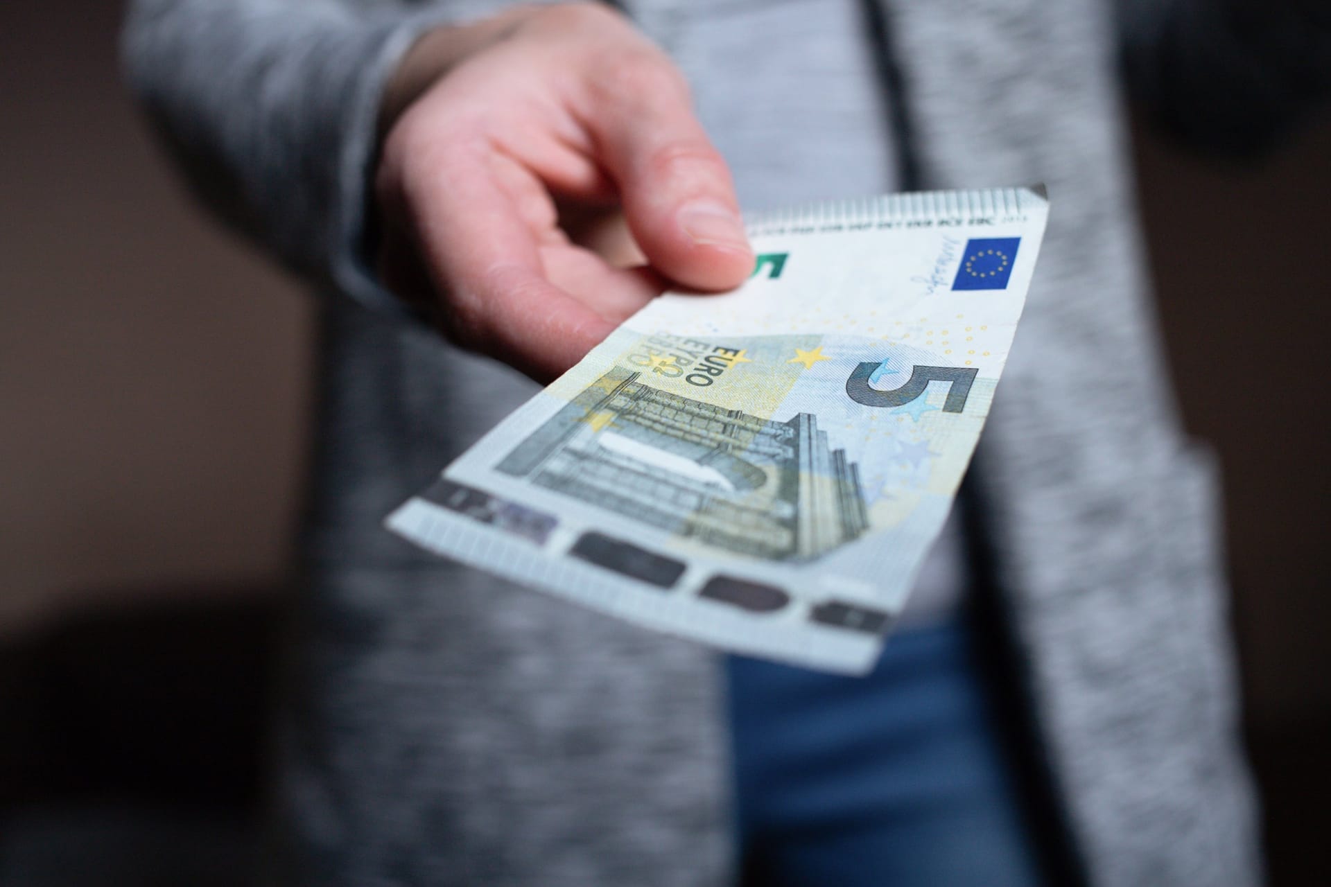 Eine Hand hält einen Fünf-Euro-Schein und reicht ihn weiter