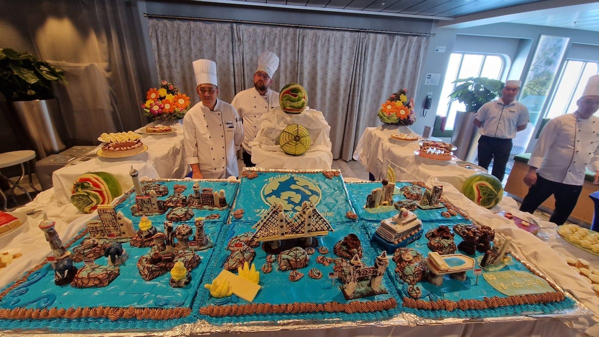 Drei Köche stehen hinter einer großformatigen, blau glasierten Torte, auf der Sehenswürdigkeiten der Reiseroute als Zuckerfiguren nachgebaut sind