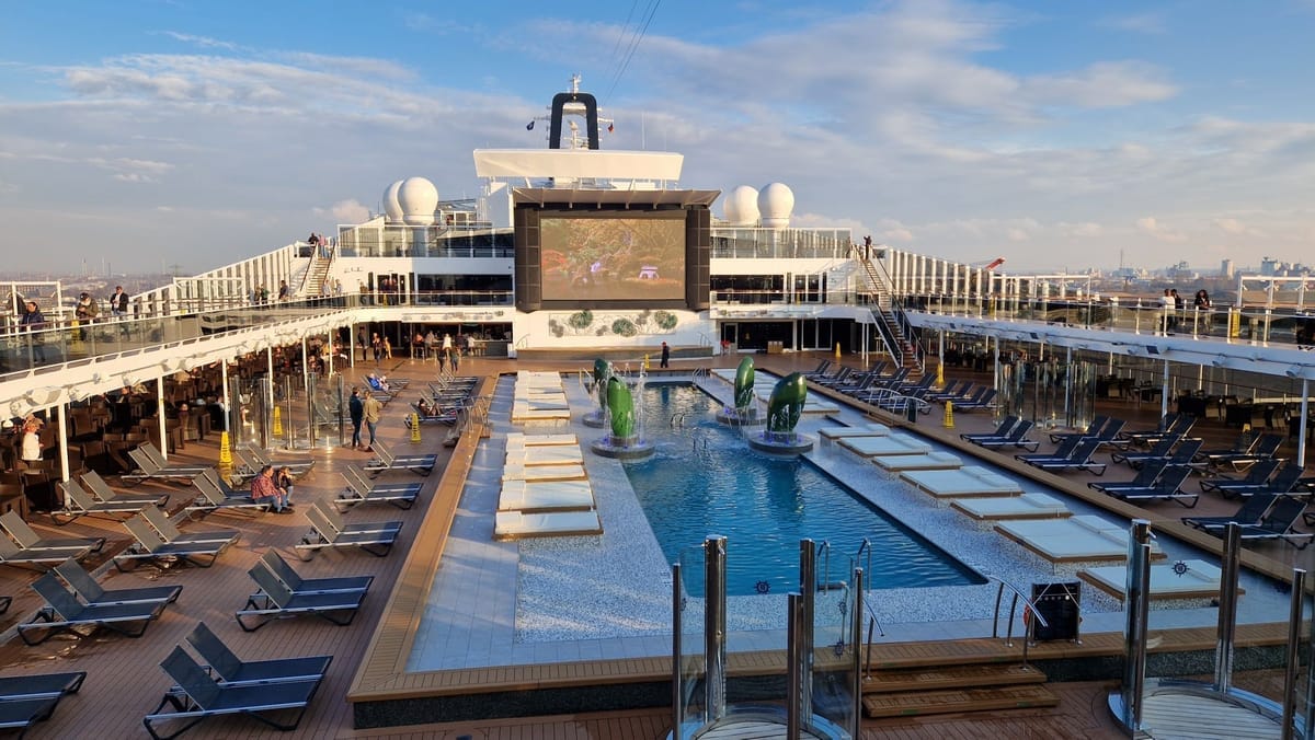 Außen-Pooldeck eines MSC-Schiffs mit Reihen von Liegestühlen, Springbrunnen-Pool und großer LED-Leinwand über dem Heck