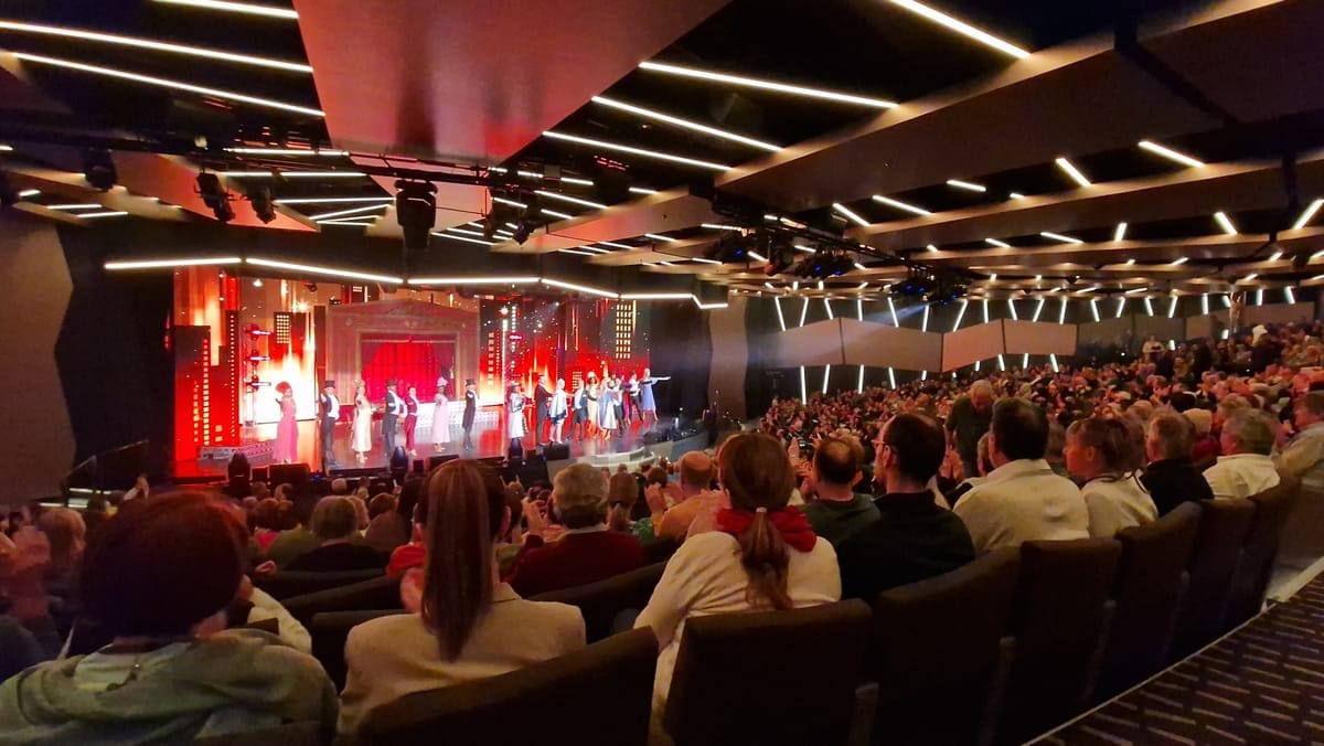 Ensemble beim Schlussapplaus auf der Bühne, davor das vollbesetzte Theater schräg von der Seite gesehen