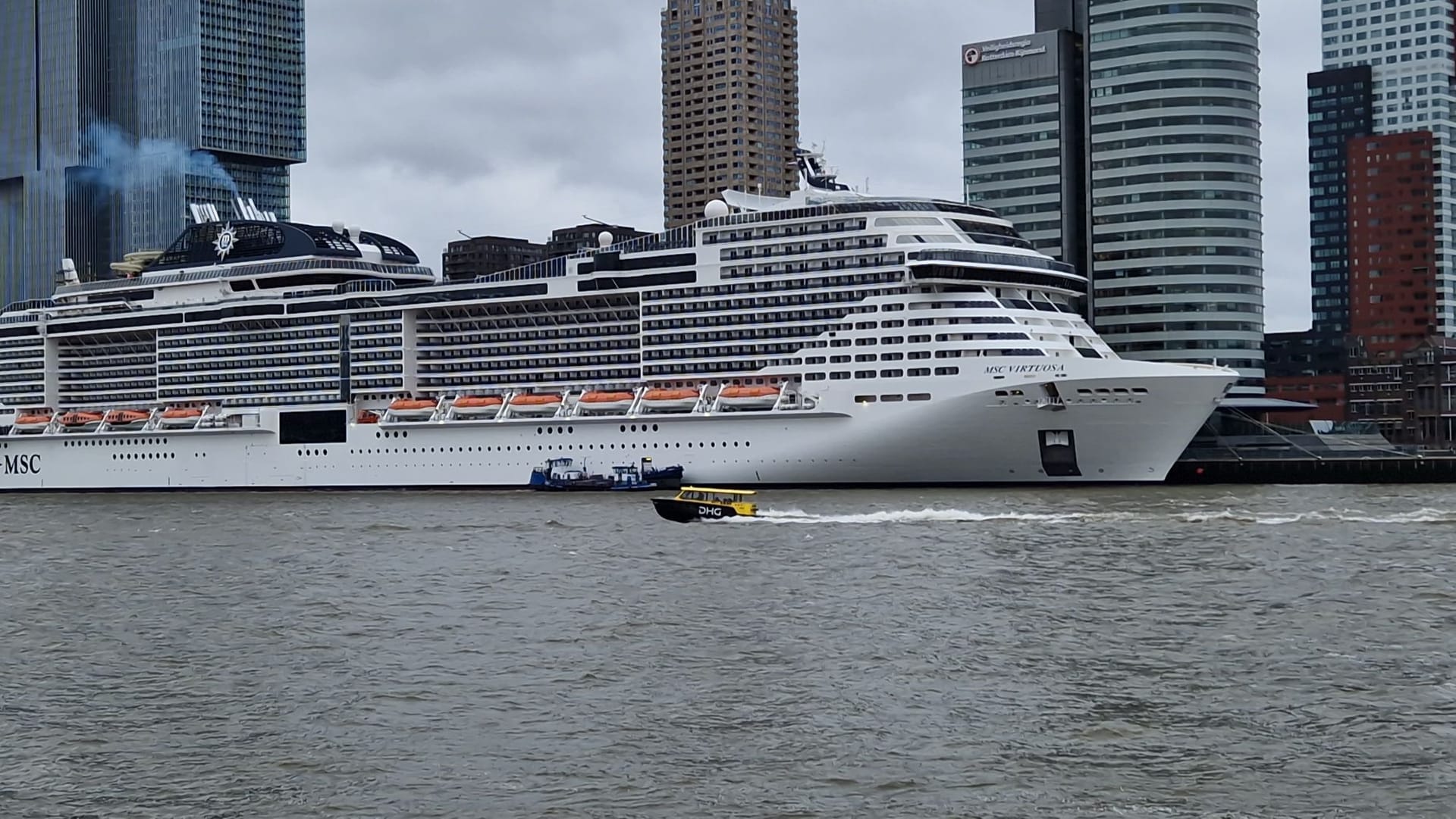 Bug der MSC Virtuosa am Kai in Rotterdam, davor ein gelbes Wassertaxi auf der Maas