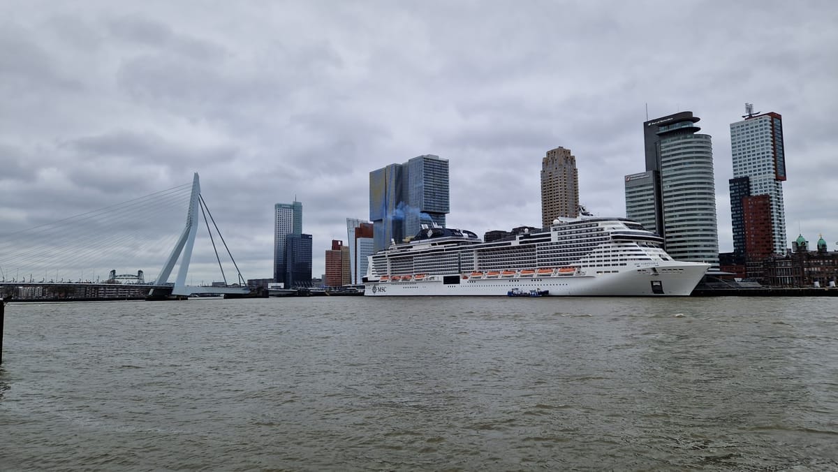 Blick über die Maas auf die Erasmusbrücke und die dahinter am Kai liegende MSC Virtuosa vor der Rotterdamer Skyline