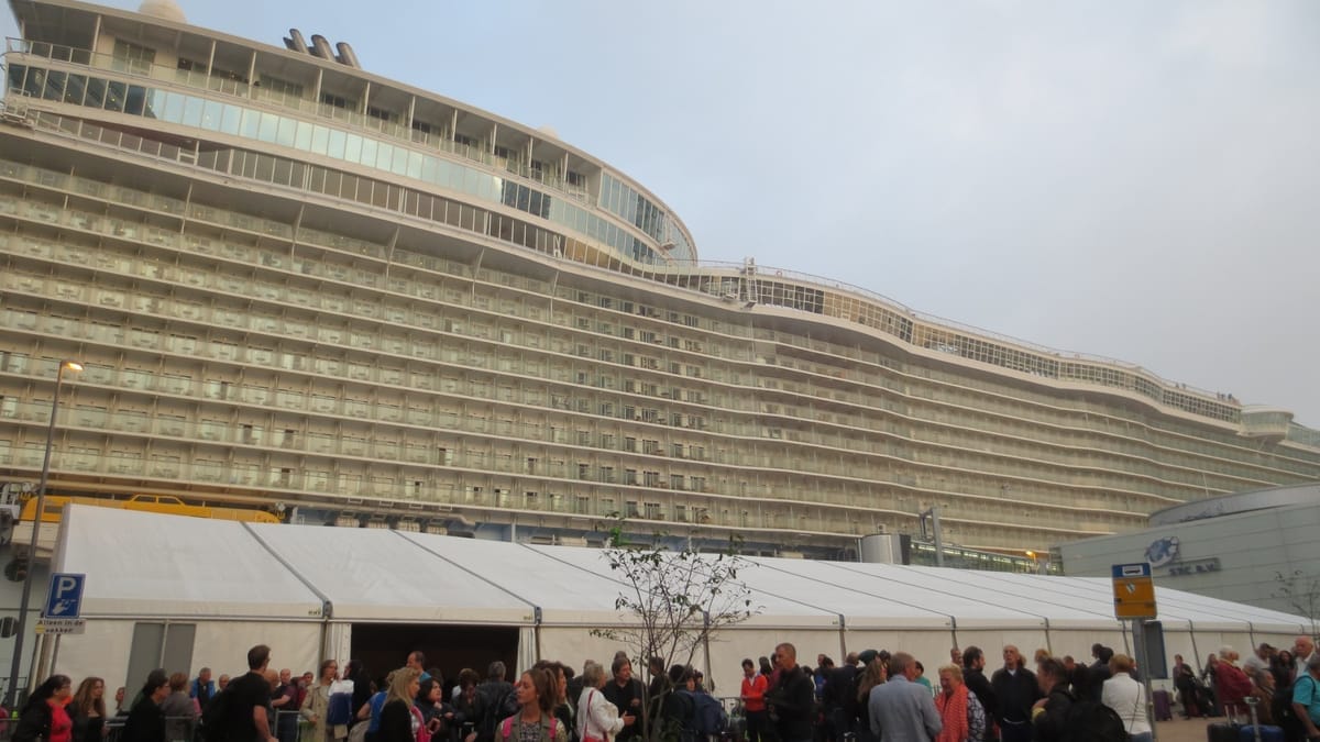 Wartende Gäste mit Koffern vor einem Zeltbau am Kreuzfahrtterminal, dahinter die Bordwand der Oasis of the Seas