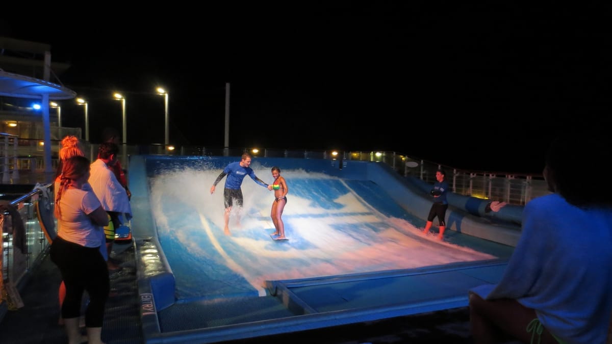 Zwei Personen auf dem FlowRider-Surfsimulator an Bord bei Nacht, Zuschauer am Rand