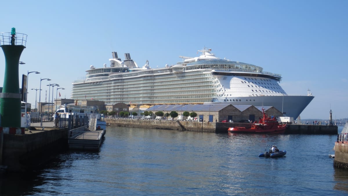 Die Oasis of the Seas hinter alten Kaischuppen, im Vordergrund ein rotes Seenotrettungsboot